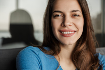 Image of woman looking at camera and smiling while sitting on sofa