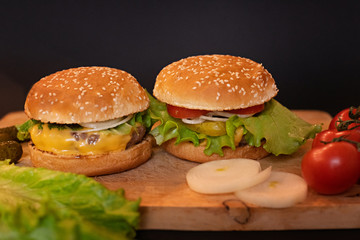several (two) homemade cheeseburgers on a wooden Board on a dark background with tomatoes and onions