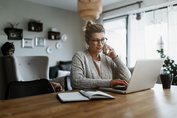 Businesswoman working on laptop computer sitting at home and managing her business via home office...