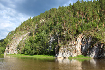 Fototapeta na wymiar A calm river that flows among the rocks. Beautiful landscape of the lake with coastal cliffs and coniferous forest, reflected in the water and atmospheric sky. Russia, river rafting, travel, wallpaper