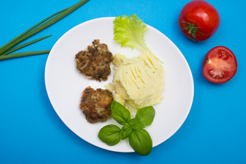 Homemade cutlets with mashed potatoes and vegetables. Top view on blue background