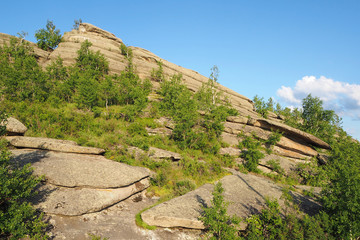 The high rock with small green trees, the blue sky with white cloud