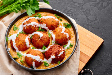 Malai Kofta Curry in black bowl at dark slate background. Malai Kofta is indian cuisine dish with potato and paneer cheese deep fried balls in onion tomato gravy with spices. Indian Food.