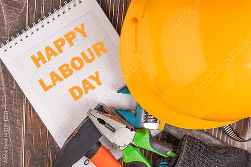 Workers' day background concept - many handy tools, notebook with happy workers' day text , wooden background, top view