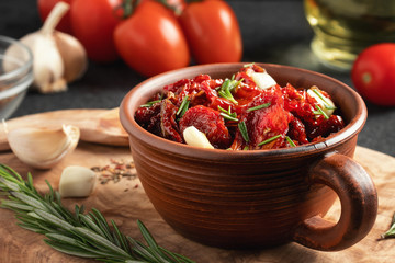 Sun-dried tomatoes with garlic, rosemary and spices in a clay bowl on an olive wood cutting board