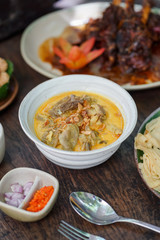 Goat curry is served in a ceramic bowl on a wooden table during a garden party.