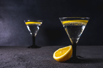 Dry martini with black olives and fresh lemon.Vermouth cocktail inside martini glass over dark background.Martini glasses are on the bar. selective focus - obrazy, fototapety, plakaty