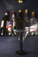 Dry martini with black olives and fresh lemon.Vermouth cocktail inside martini glass over dark background.Martini glasses are on the bar. selective focus