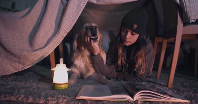 Adolescente con perro Golden Retriever leyendo debajo de una tienda improvisada