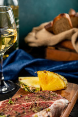 Raw meat on a wooden board with pineapple and a glass of wine