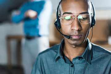 Focused African American man with headset looking down. Front view of call center operator. Call...