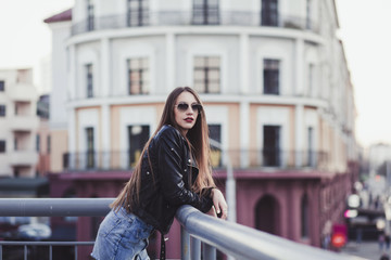 beautiful woman in sunglasses and leather jacket against the background of city life