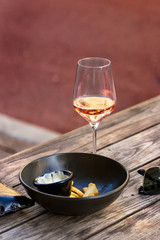 A red - rose wine glass placed on a wooden table next a bowl with leftovers, outdoors.