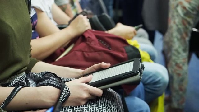 Woman reads e-book holding a bag in subway train at metro on the backgrounds of other seating people.