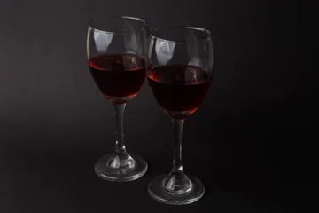 Fotobehang hermosas copas de vino transparentes con vino tinto sobre un fondo negro © Arvin
