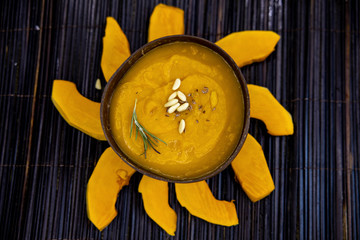 Roasted pumpkin and carrot soup with rosemary and pumpkin seeds on wooden background, on burlap. Copy space