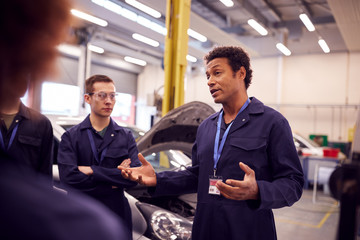Male Tutor With Students Teaching Auto Mechanic Apprenticeship At College