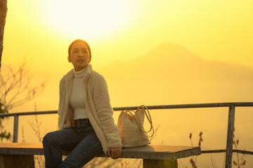 Fototapeta premium tourist women in white shirt and jeanes sit bench in relaxing Emotional The winter with blur background mountain sunrise in the morning at Phutok hill view point, Chiangkhan, Loei Province, Thailand.