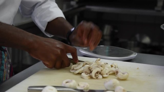 D&eacute;coupe de champignons de Paris par une personne de couleur dans une cuisine professionnelle