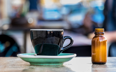 Close-up of a black coffee cup with a small bottle with milk on the side, placed on a wooden table over blurred people background.