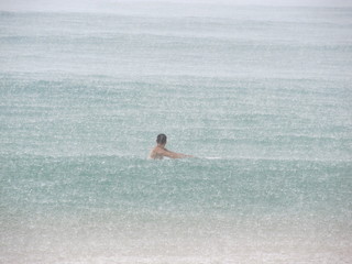 Young man swims on a surfboard in the ocean in the rain.