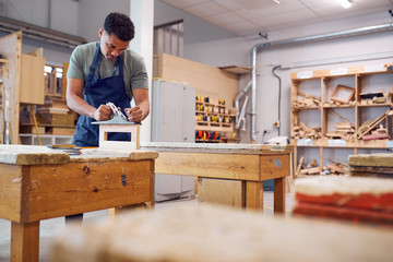 Male Student Studying For Carpentry Apprenticeship At College Using Wood Plane