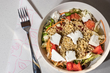 Top view of a greek salad bowl with cracked wheat, tomatoes, lettuce and feta chesse.