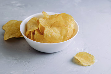 Salted spicy potato chips in a plate on a gray background with place for text side view