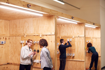 Female Tutor With Trainee Electricians In Workshop Studying For Apprenticeship At College