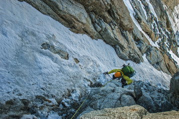 Climber on a steep snow-ice slope with an ice ax. Alps.