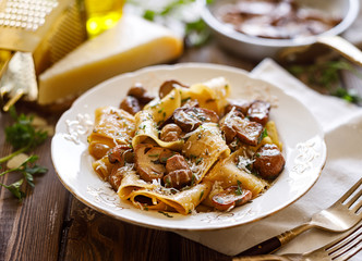 Pappardelle pasta with porcini mushrooms, sprinkled with parmesan cheese and chopped parsley in a ceramic plate on a wooden table, close up. 