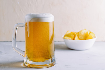 Light beer in a large glass with froth and bubbles and potato chips side view