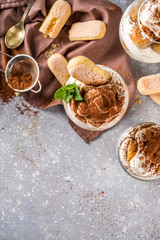Traditional italian dessert tiramisu. Many glasses with homemade tiramisu with chocolate cocoa powder, grey stone stone or concrete background.