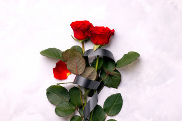 two red roses tied with a black mourning ribbon on a gray marble background. concept of sorrow and death