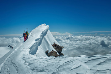 Two guys ski mountaineeres go to the top along a fantastic ridge with a snow cornice. Sea of clouds...