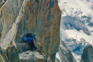 Cautious climber with a rope on a steep cliff. Huge cracked glacier with great bergschrund