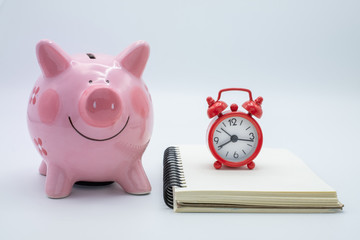 Pink piggy bank Expense Book And red alarm clock The idea of saving money to buy a house for the future, accumulating a small amount of money. Retirement money The time to save money.