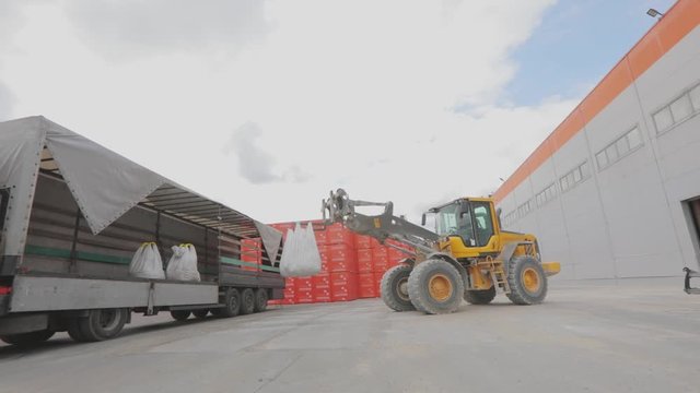 A bulldozer loads bags into a truck. Loading goods into a truck