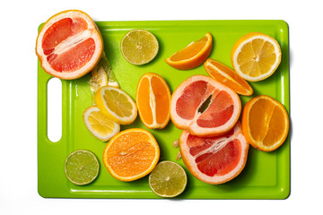 Slices and halves of lemon, lime, orange and grapefruit on a green chopping board. Multiple kinds of citric together.  