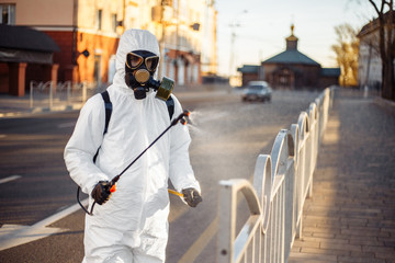 Disinfection team worker is cleaning pavement fence with a sterilizing water spraying it over the coronavirus infected surface. Covid-19 protective equipment and actions to stop spread of the disease.