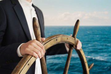 Businessman holding ship rudder and navigates in ocean.