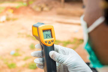 young black lady holding a handheld infrared thermometer to read the temperature on it