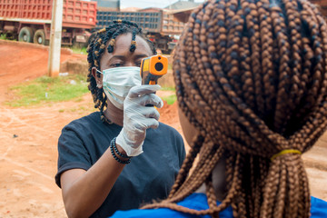 young black lady using a handheld infrared thermometer to test a lady's temperature