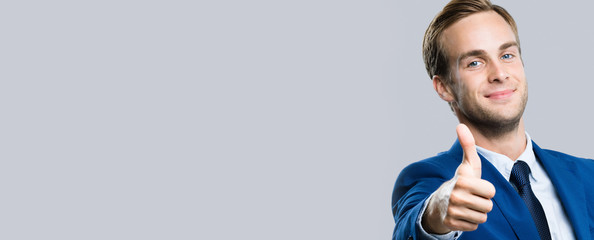 Portrait of smiling attractive businessman showing like gesture, over grey background. Business...