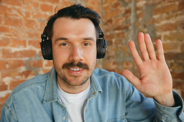 Caucasian musician in headphones greeting audience before online concert or sound-check at home isolated and quarantined, looks cheerful, smiling. Concept of art, support, music, hobby, education.