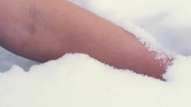 CU, slow motion: mature woman dips bare hand with manicure and red thread into deep white snow and takes arm out extreme closeup