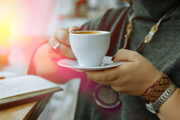 A woman holds a cup of coffee on the background of her laptop and notebook.