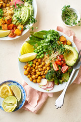 Healthy vegetarian lunch bowl with avocado, chickpeas, quinoa and vegetables, garnished with microgreens and nut dressing. Flat lay on stone background.