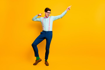 Fototapeta na wymiar Full length photo of cool stylish guy boyfriend dancing festive mood excited direct finger side wear specs shirt bow tie suspenders trousers shoes isolated vivid yellow color background