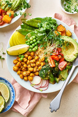 Healthy vegetarian lunch bowl with avocado, chickpeas, quinoa and vegetables, garnished with microgreens and nut dressing. Flat lay on stone background.